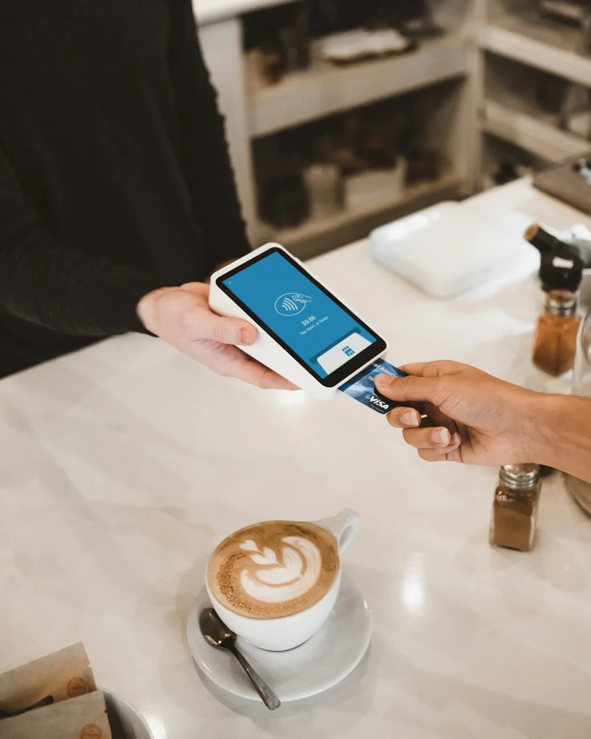 A card being tapped on a small payment terminal held over a shop counter