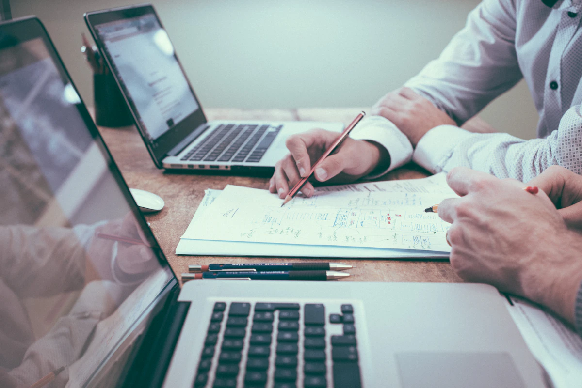 Two people reviewing a project plan together at a desk, comparing notes before committing